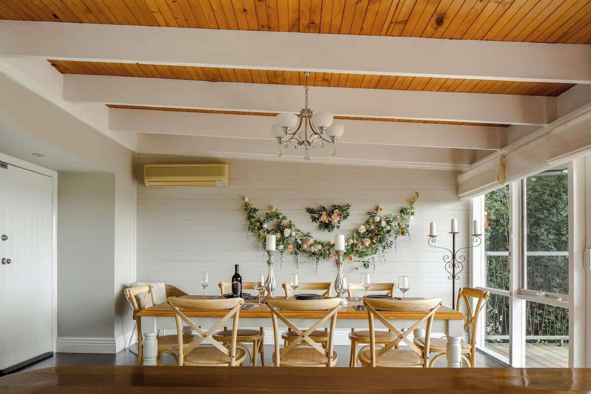 Un comedor con mesa y sillas de madera, una araña y un adorno floral en la pared.