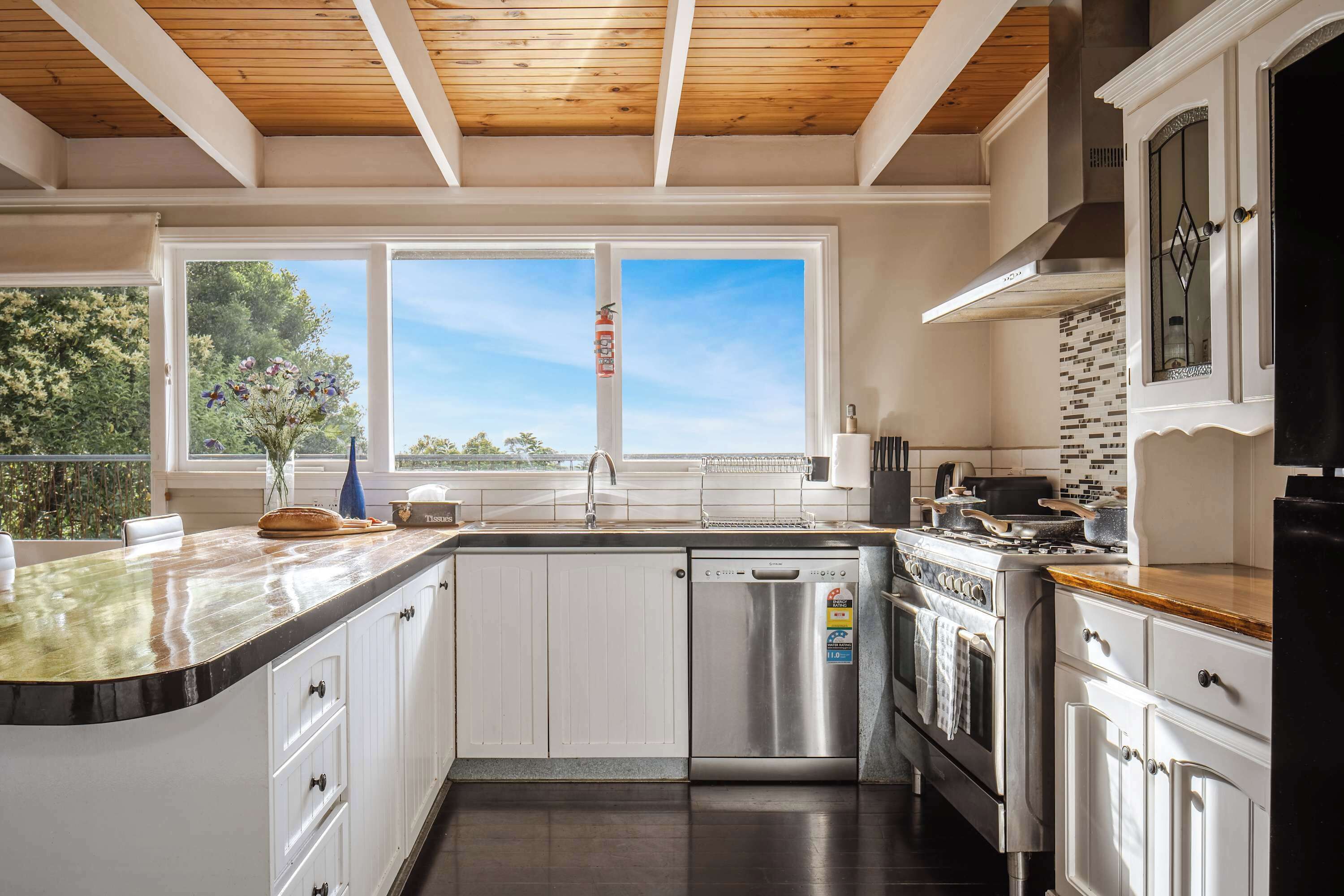 Una cocina moderna con armarios blancos, lavavajillas de acero inoxidable y un ventanal con vistas a árboles.