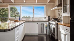 A modern kitchen with white cabinets, a stainless steel dishwasher, and a large window with a view of trees. - Seednest Treehouse Spectacular Mountain View (Monbulk)