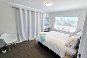 A bedroom with a bed, a chair, a nightstand, a window with blinds, and a painting on the wall.