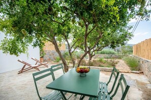 Ein grüner Tisch mit Obstschale, umgeben von grünen Stühlen, unter einem Baum mit grünen Blättern.