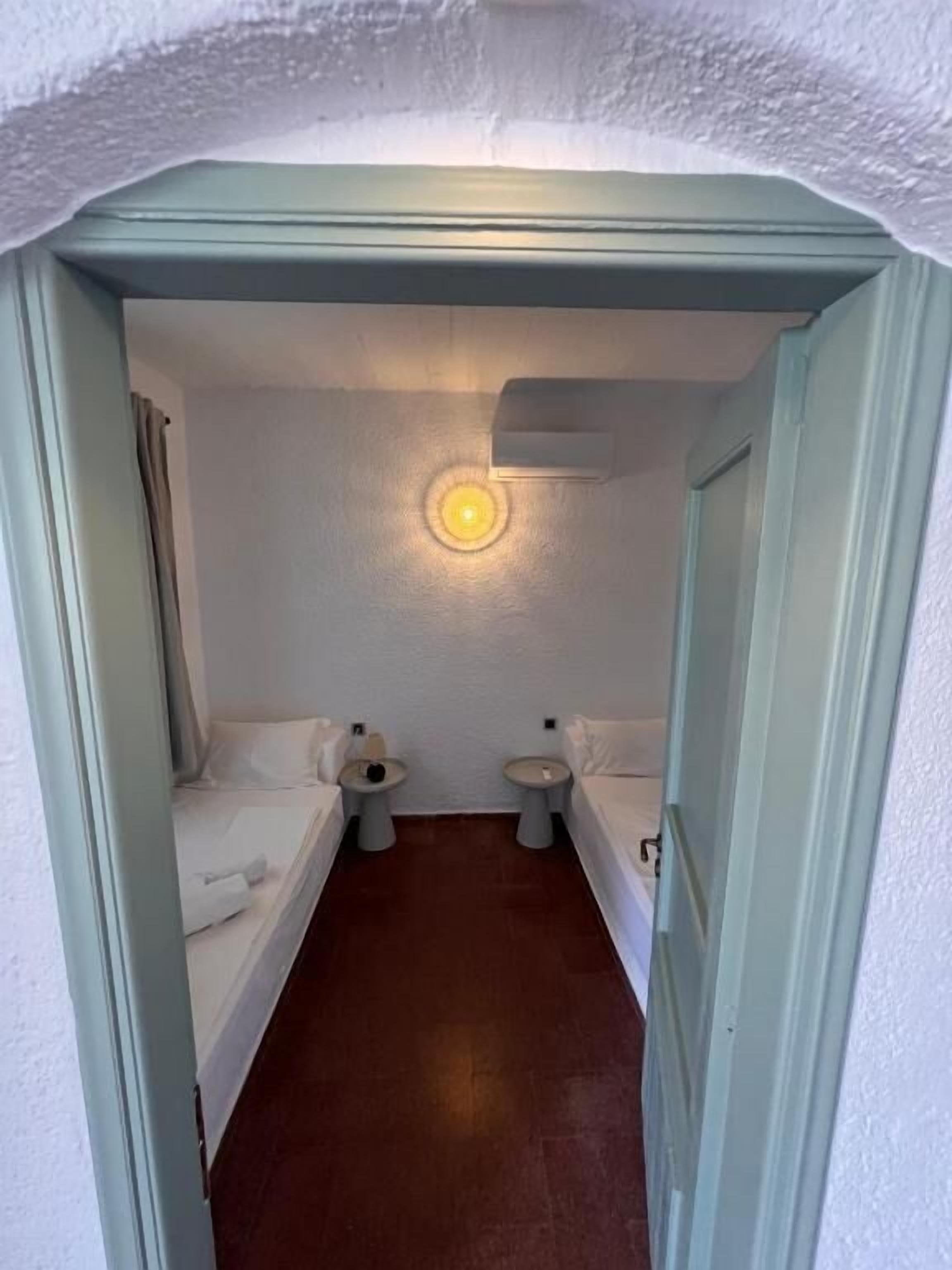 A narrow, dimly lit room with a single bed, two bedside tables, and a small window.