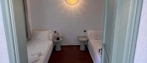 A narrow, dimly lit room with a single bed, two bedside tables, and a small window.