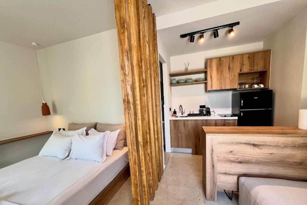 Een kleine kamer met een bed, een houten scheidingswand, een kitchenette en een eethoekje.
