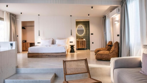 Een moderne hotelkamer met een groot bed, een zithoek met een bank en fauteuil, een kleine tafel en uitzicht op de stad.