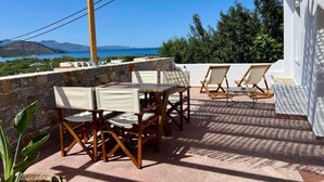 Een terras buiten met een tafel en stoelen, een pergola met hangende decoraties, en uitzicht op zee en heuvels.