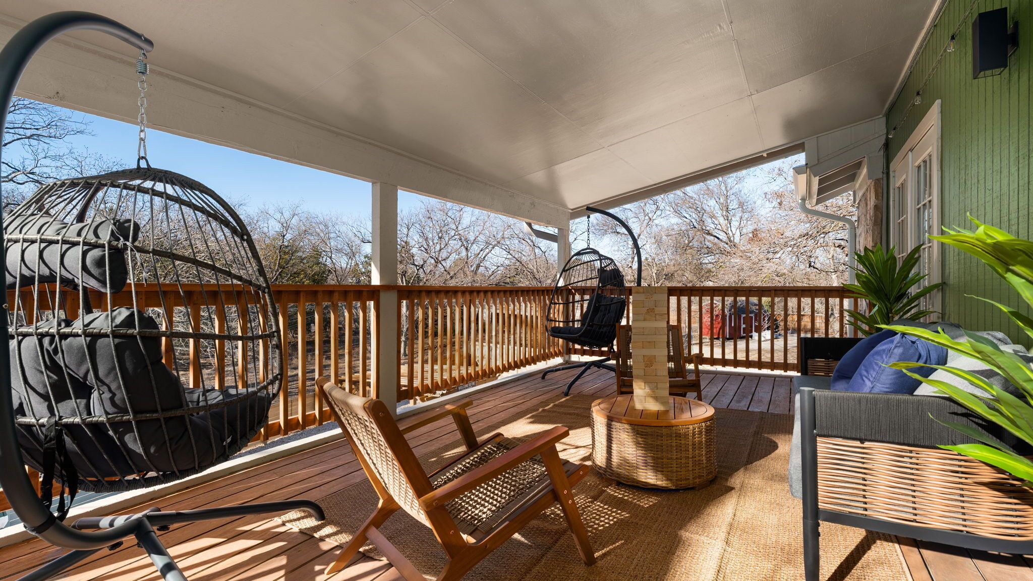 A covered outdoor deck with a swing chair, a cushioned chair, and a wicker table.