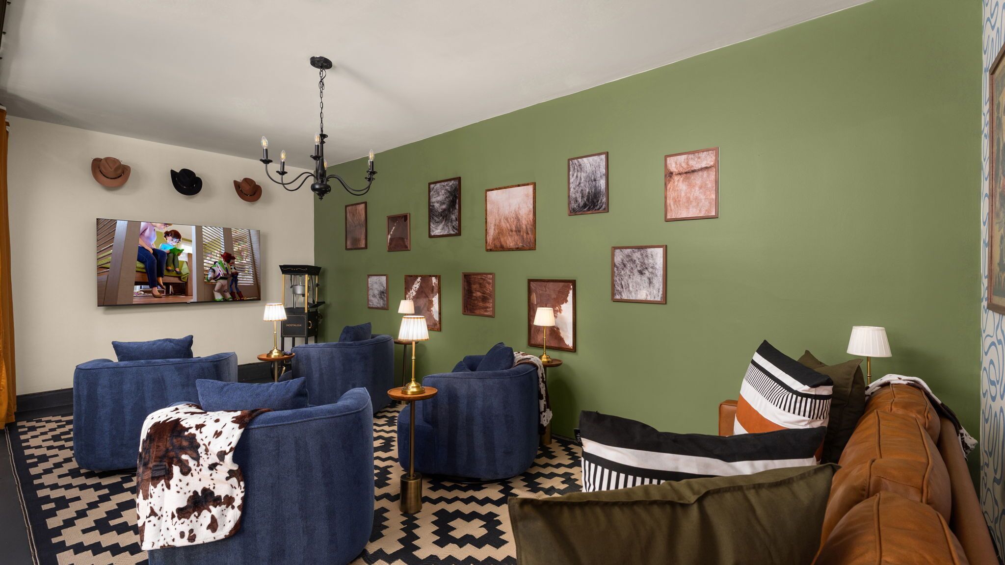 A living room with a green wall, multiple framed artworks, a chandelier, and a variety of seating including sofas and a couch.