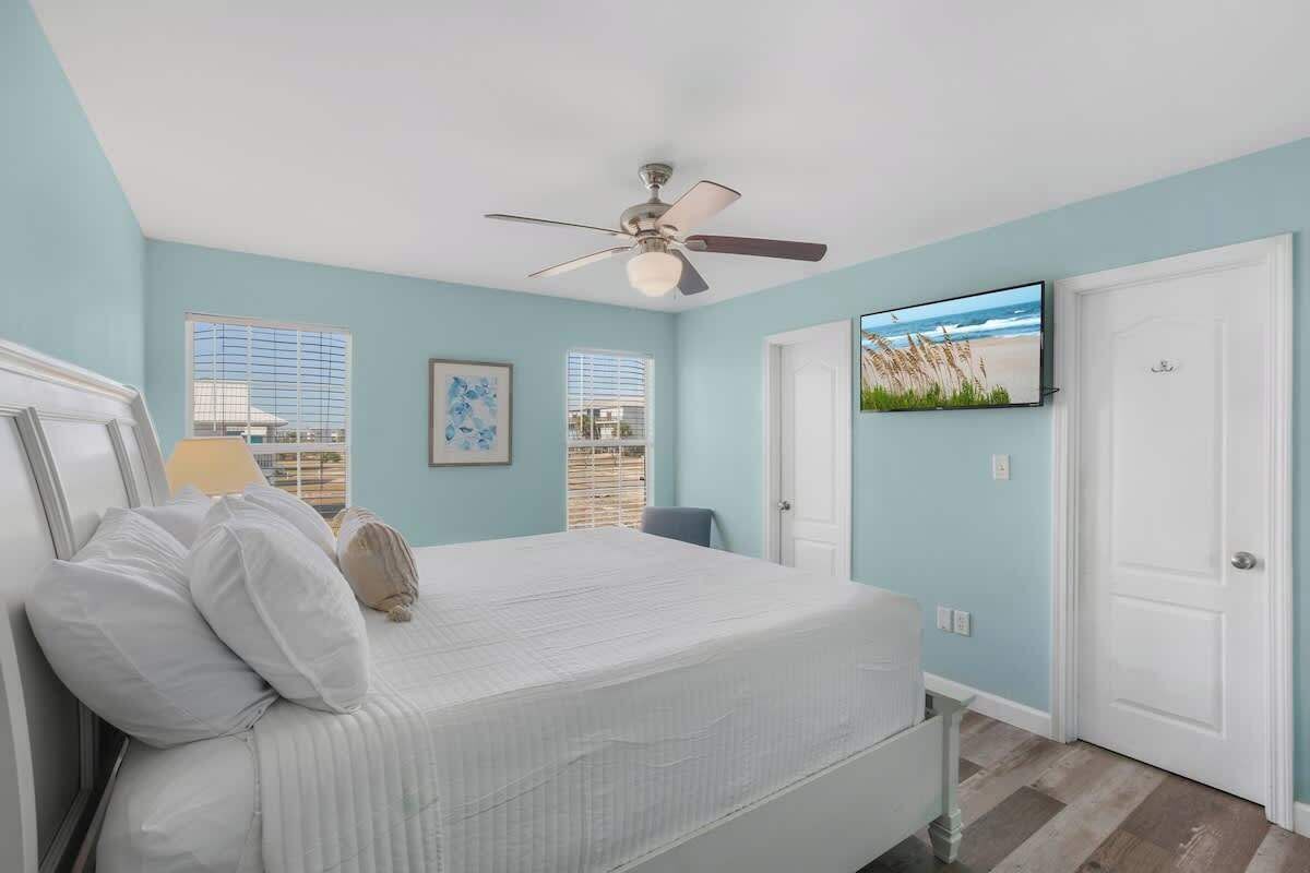 Ein Schlafzimmer mit Bett, Deckenventilator, Fernseher an der Wand und einer Tür.
