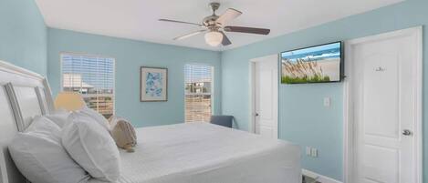 Ein Schlafzimmer mit Bett, Deckenventilator, Fernseher an der Wand und einer Tür.