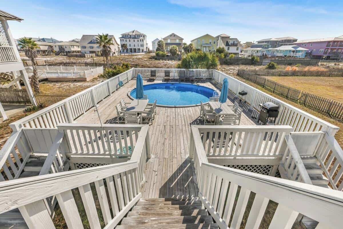 A wooden deck with a pool, surrounded by white railings and palm trees.