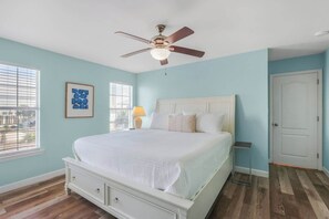 Een slaapkamer met een bed, een plafondventilator, een raam met jaloezieën en een deur.