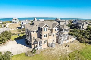 A multi-story residential building with a spacious driveway and a view of the ocean. - Gertrude's Breakaway - Corolla, Ocean View, 45 Yds to Beach, Elevator, Pool, Tiki Bar, Hot Tub (Corolla)