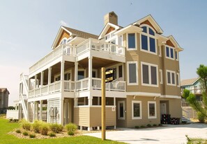 A multi-story house with a balcony, a garage, and a driveway. - Gertrude's Breakaway - Corolla, Ocean View, 45 Yds to Beach, Elevator, Pool, Tiki Bar, Hot Tub (Corolla)