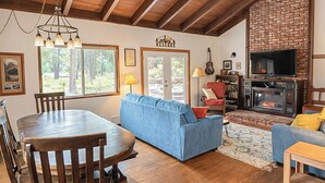 A spacious living area with a wooden ceiling, a fireplace, a dining table with chairs, and a blue sofa. - Sunriver retreat w/ hot tub, SHARC passes, pet-friendly (Sunriver)
