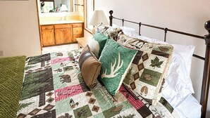 A bedroom with a wooden ceiling, a bed with a quilt, a nightstand, a mirror, and a window. - Sunriver retreat w/ hot tub, SHARC passes, pet-friendly (Sunriver)