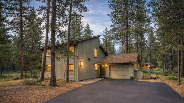 A two-story house with a garage, surrounded by tall pine trees. - Sunriver retreat w/ hot tub, SHARC passes, pet-friendly (Sunriver)