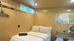 Ein Schlafzimmer mit Bett, Schreibtisch, Stuhl, einer Karte an der Wand und einem Fenster.