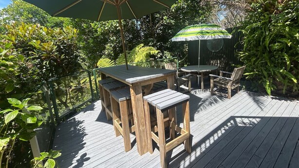 Eine Holzterrasse mit Gartenmöbeln, darunter ein Tisch und Stühle, unter einem großen Sonnenschirm.
