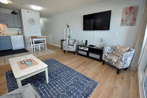 A compact living space with a dining area, a sofa, a TV, and a kitchen area. - Sea Mystique 204 - Oceanfront Condo in Garden City Beach (Garden City)