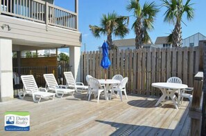 Une terrasse extérieure avec des chaises et une table en plastique blanc, une plateforme en bois et une clôture en bois.