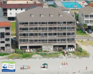 A multi-story hotel with balconies, located near a beach with people sunbathing and a pool in the background. - Sea Mystique 204 - Oceanfront Condo in Garden City Beach (Garden City)