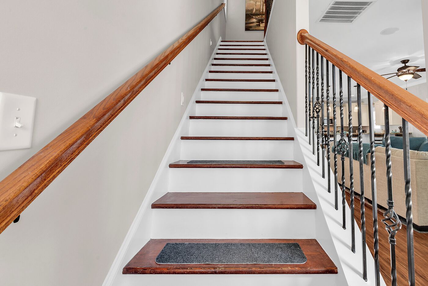 Una escalera con barandas de madera y un pasamanos de metal, que lleva a un rellano con una puerta.