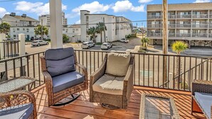 A balcony with wicker furniture and a view of a parking lot and buildings. - The Salty Mermaid - Walk to Garden City Beach (Garden City Beach)