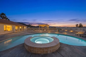 Una piscina con hidromasaje, una zona de estar techada y un patio cercado.