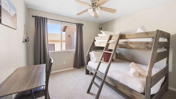 A room with a bunk bed, a desk, a chair, a ceiling fan, and a window with curtains. - Casa Selecta - Hot Tub, Game Room & Pool (Yucca Valley)