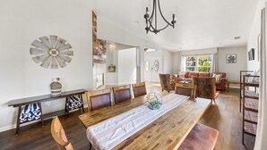 A dining area with a long wooden table, multiple chairs, a chandelier, and a decorative wall piece. - Casa Selecta - Hot Tub, Game Room & Pool (Yucca Valley)