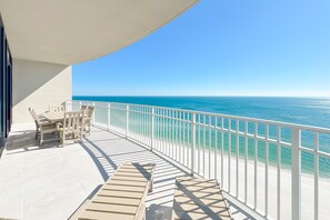En balkon med udsigt over havet, et bord med stole og en liggestol.