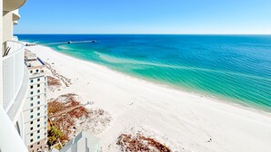 Une vue sur la plage depuis le balcon d’un hôtel, avec un ciel dégagé, une plage de sable et une jetée qui s’avance dans l’océan.