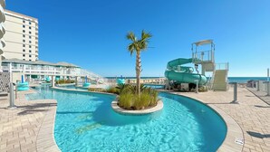 Une piscine avec un palmier, un toboggan aquatique et une vue sur l’océan.