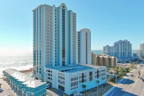 Ein Hochhotel mit zahlreichen Stockwerken, einem markanten Logo obenauf und Blick auf Strand und Meer im Hintergrund.