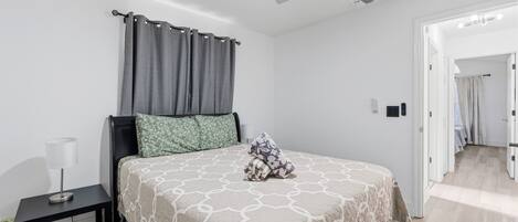A bedroom with a bed, a nightstand, a lamp, a ceiling fan, and a door leading to another room.