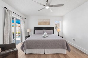 Ein Schlafzimmer mit einem Bett, zwei Nachttischlampen, einem Deckenventilator und Blick auf einen Swimmingpool.