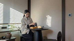 A person at a table with a teapot, cups, and a bowl, in a room with a plant, a thermostat, and a small electronic device on the wall. - Anook Hotel & Spa Seoul Jongno Anguk 2nd (Seoul)