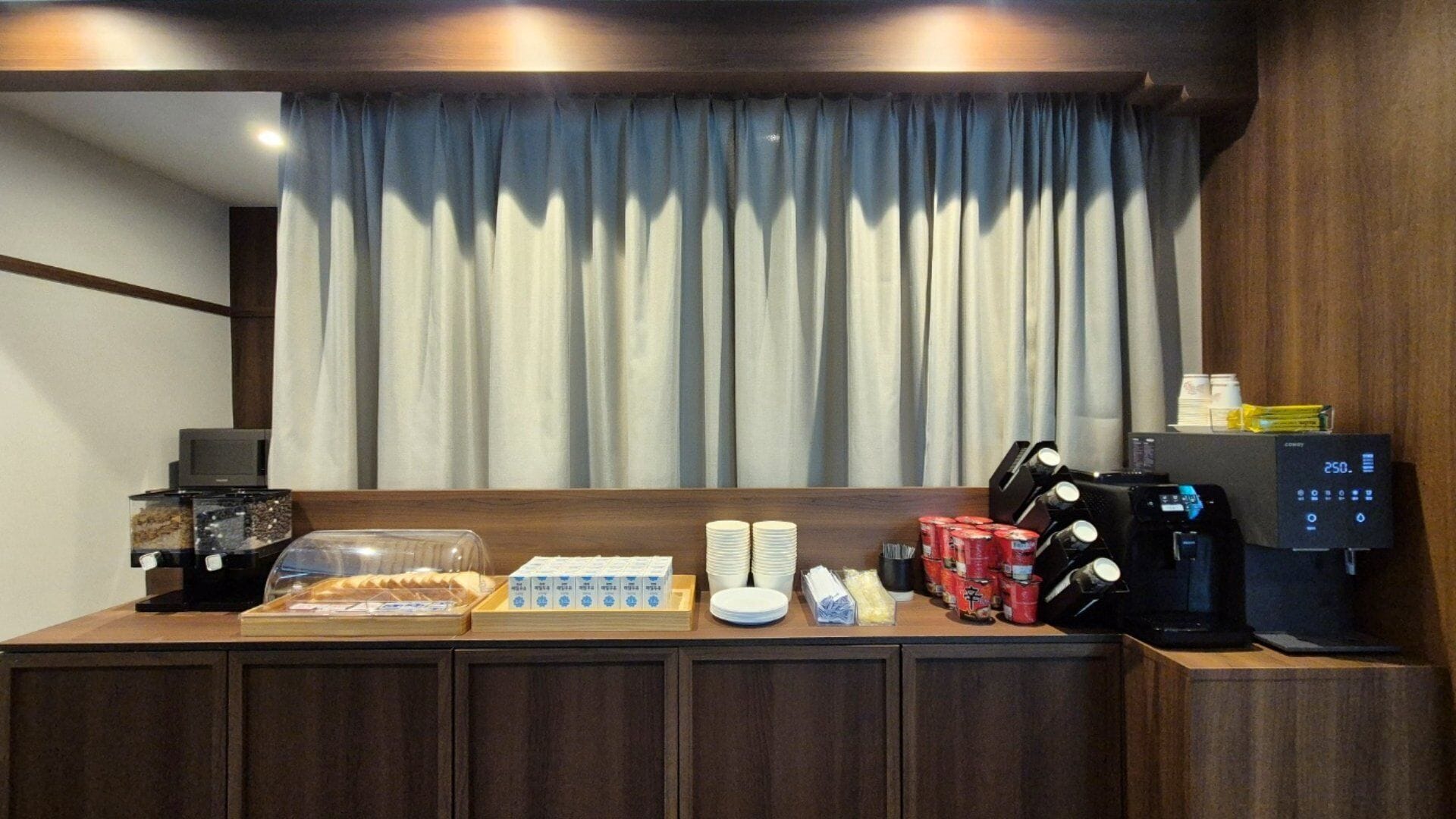 Un espace d’accueil d’hôtel comprenant un coin café avec une machine à café, des tasses et un présentoir pour les aliments.