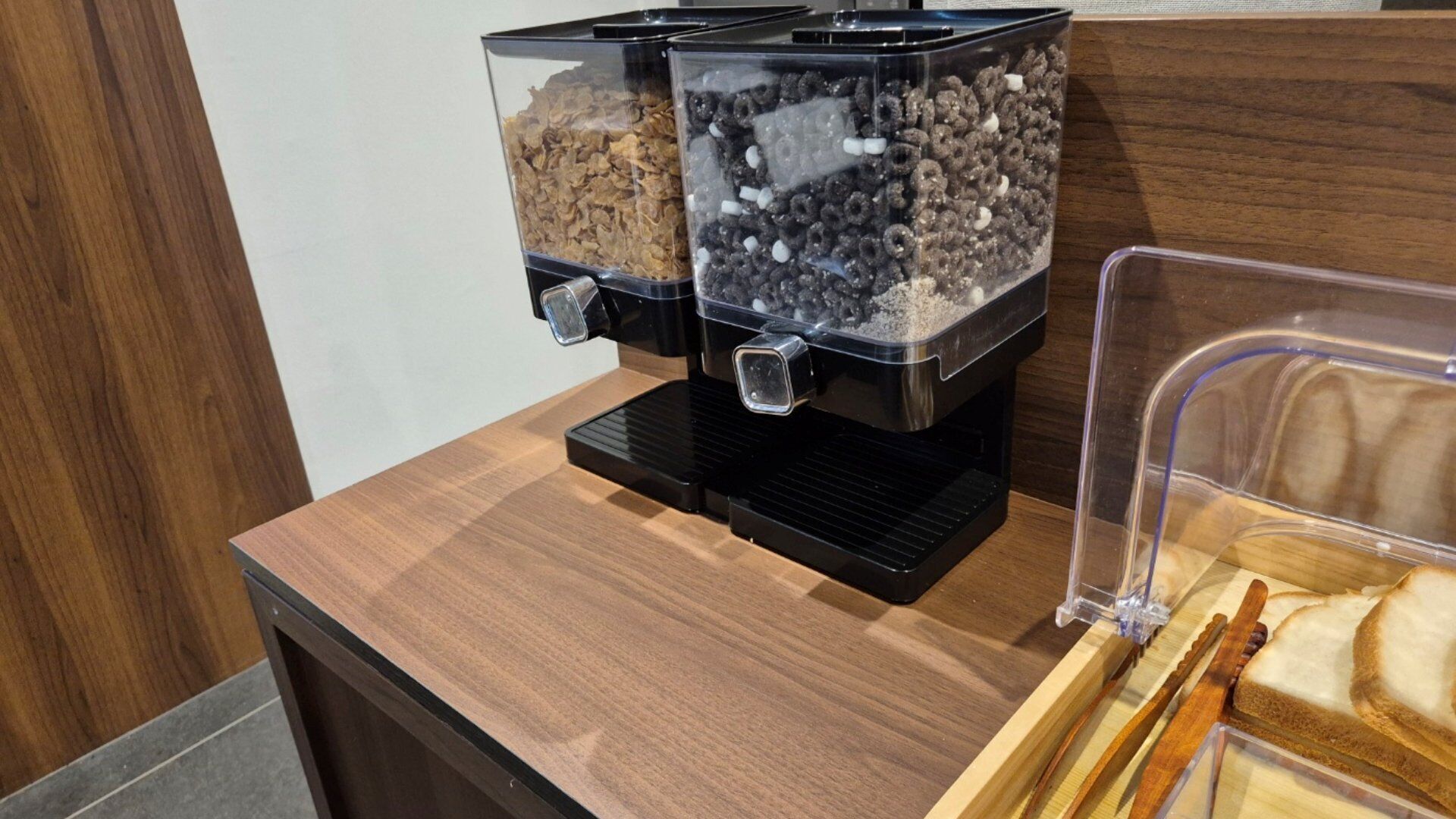 A coffee station with two dispensers, one with cereal and the other with nuts and chocolate.
