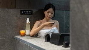 A person using a smartphone at a counter with a caution sign, a candle, and a bottle. - Anook Hotel & Spa Seoul Jongno Anguk 2nd (Seoul)
