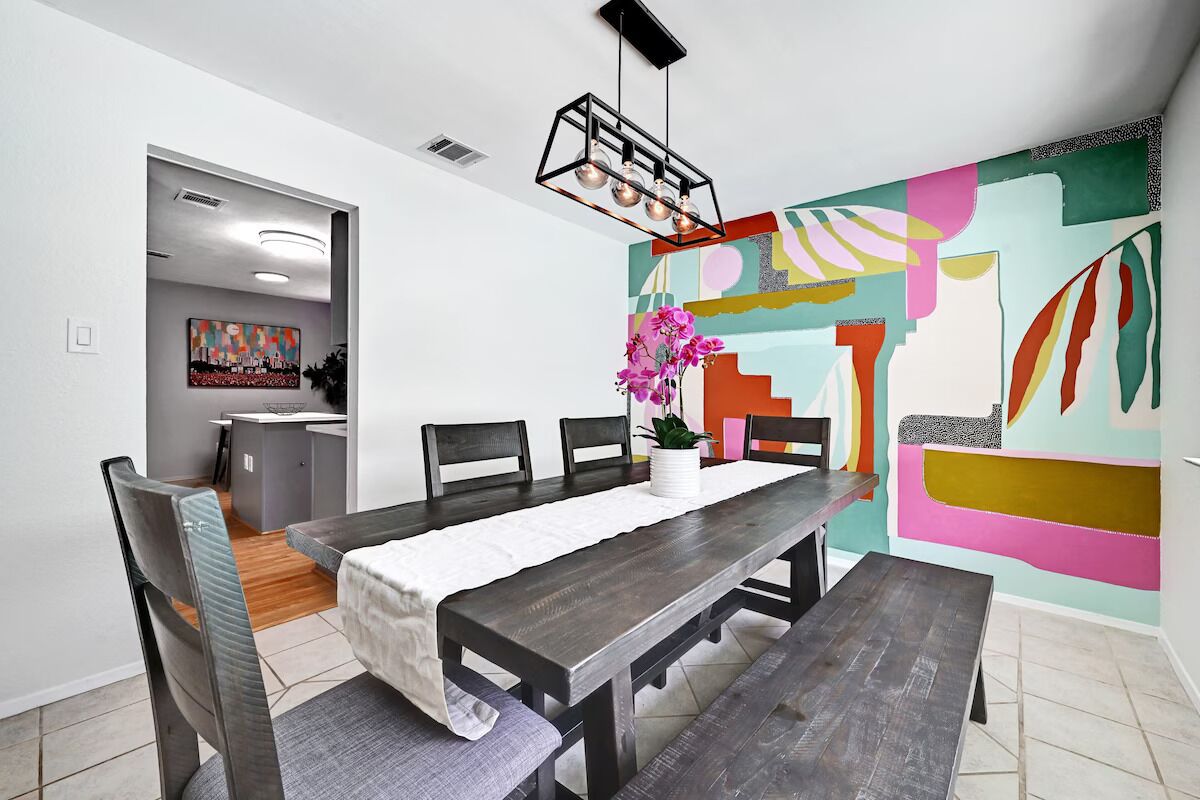 A dining area with a wooden table, chairs, and a colorful abstract painting on the wall.