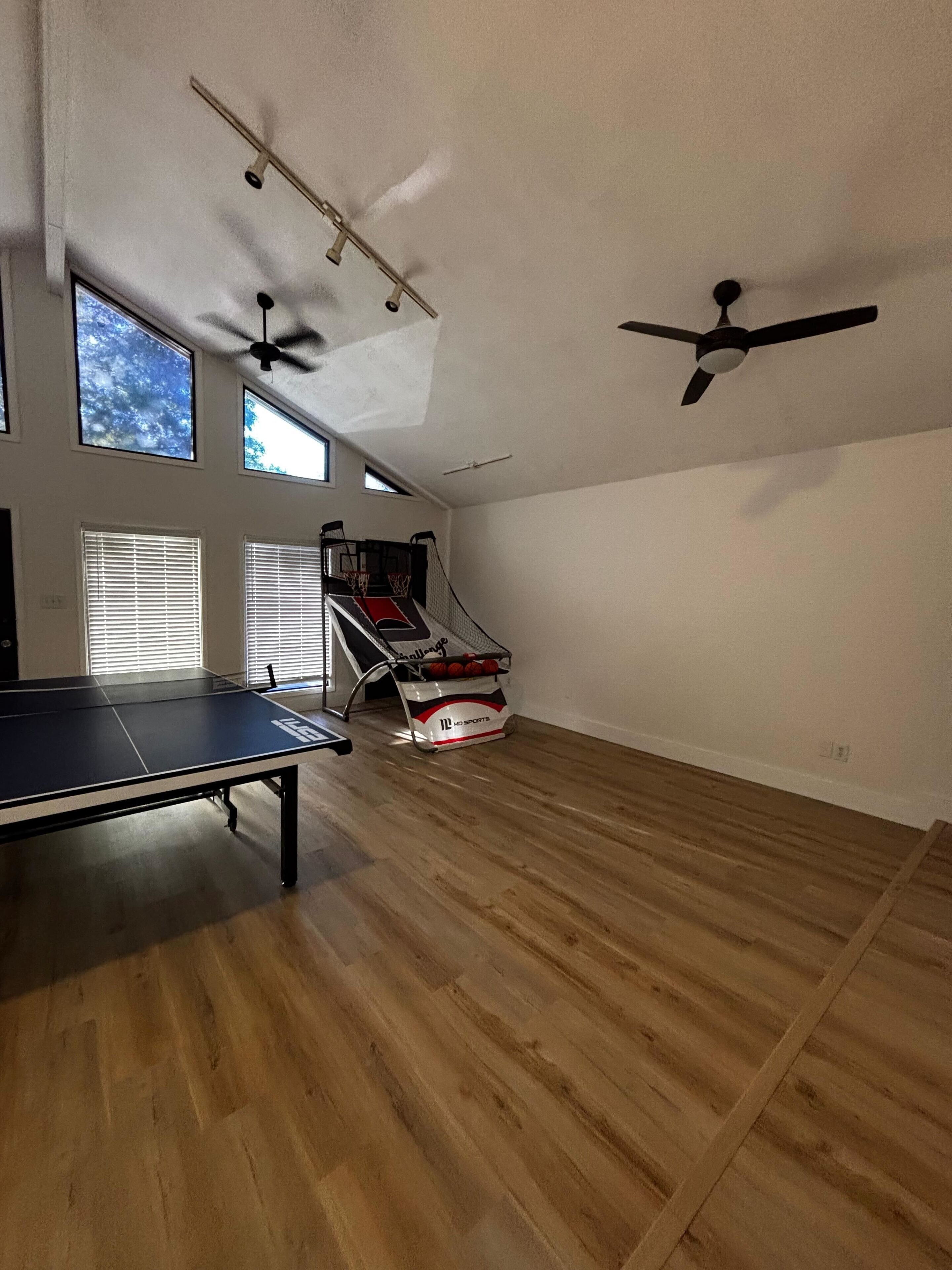 A spacious room with a ping pong table, ceiling fans, and a basketball hoop.