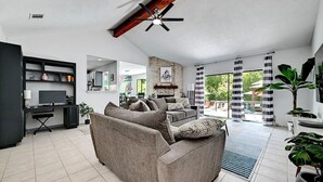 Ein modernes Wohnzimmer mit Sofa, Fernseher, Kamin und einem großen Fenster mit Vorhängen.