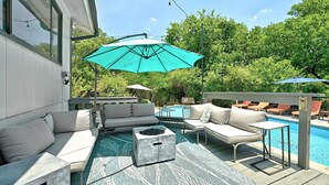 Eine Außenpatio mit Pool, einer Sitzecke mit einer Couch und Sesseln sowie einem großen Sonnenschirm, der Schatten spendet.