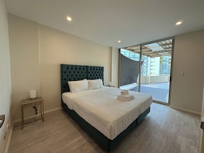 Un hotel moderno con una cama grande, una mesita de noche pequeña y vistas al exterior a través de una puerta de cristal.