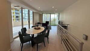 Un moderno comedor con una mesa redonda y sillas, ventanas amplias y vista a un paisaje urbano.