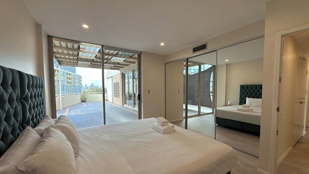 Una habitación de hotel moderna con una cama grande, un dormitorio separado y una puerta corrediza de vidrio que da a un balcón.
