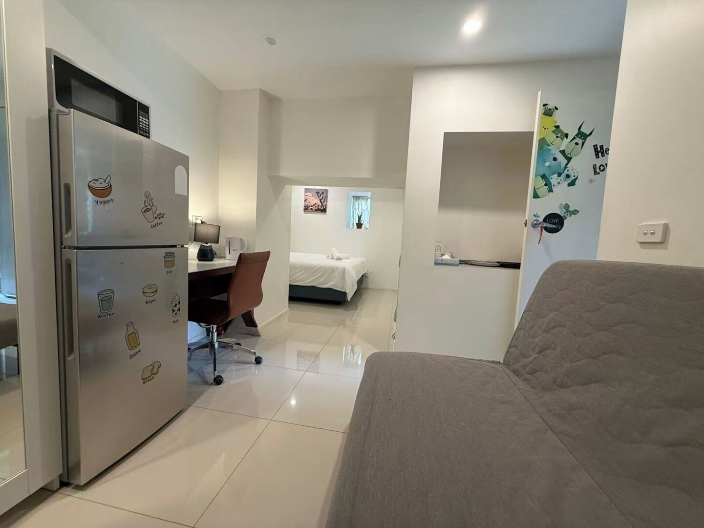 A compact hotel room with a kitchenette, a bed, a desk, and a small bathroom.