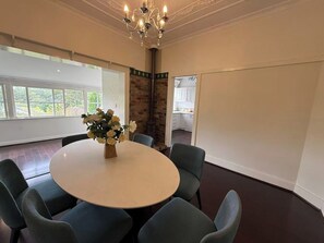 A conference room with a round table, six chairs, a vase of flowers, a chandelier, and a view of the outdoors through large windows.